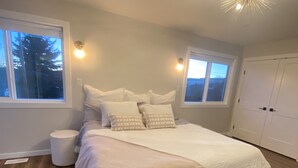 A bedroom with a large bed, two windows, a ceiling light fixture, and a wardrobe. - Modern Oasis (Prince George)