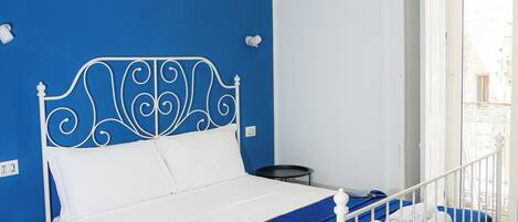 A bedroom with a white metal bed frame, a blue wall, and a wooden floor.