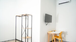 A room with a wooden desk, a chair, a TV mounted on the wall, and a metal shelving unit. - Vulcania Rooms (Naples)