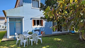 A blue house with a small patio, white plastic chairs, and a table.