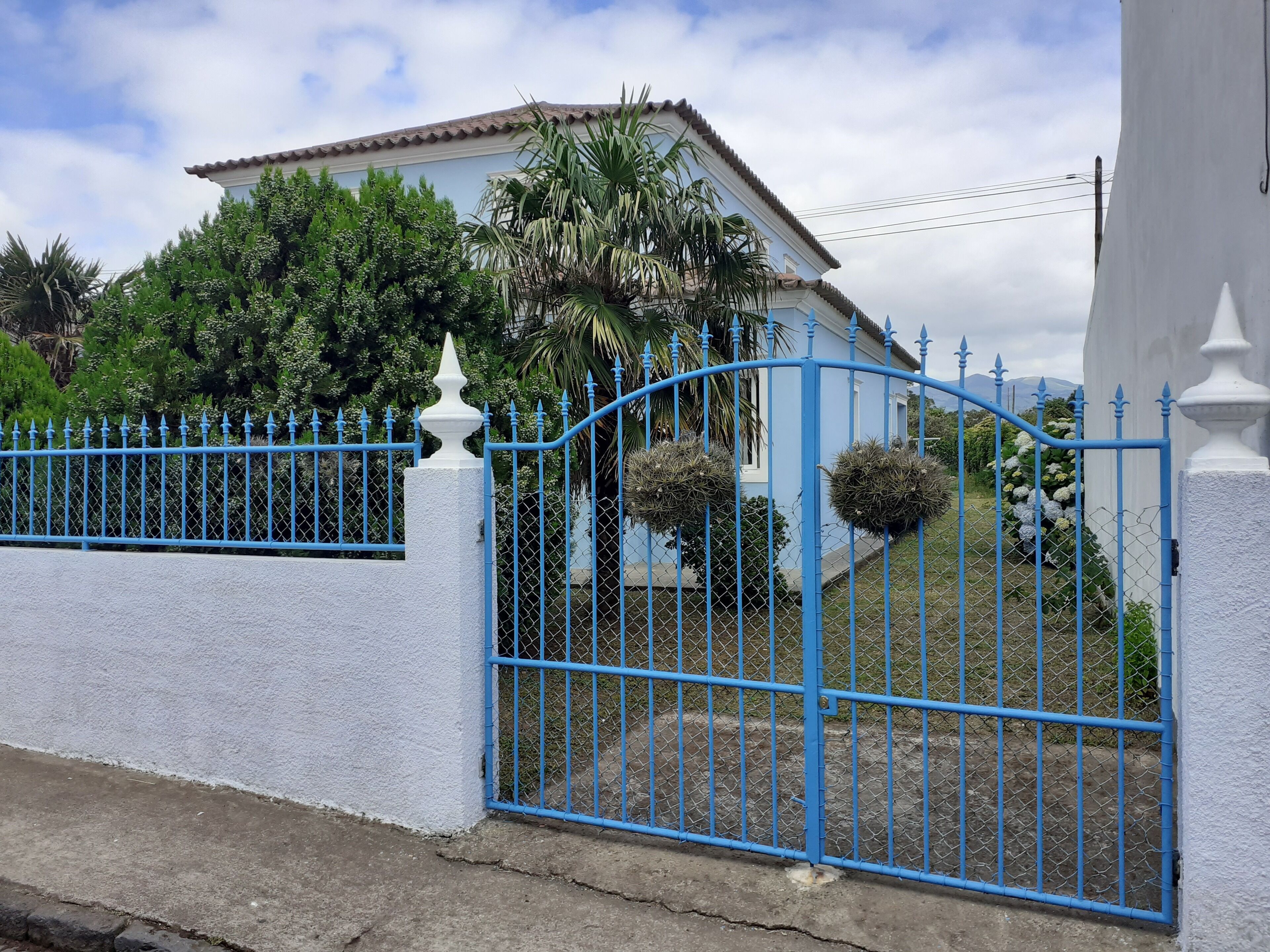 A house with a blue metal gate, white walls, and a tiled roof.