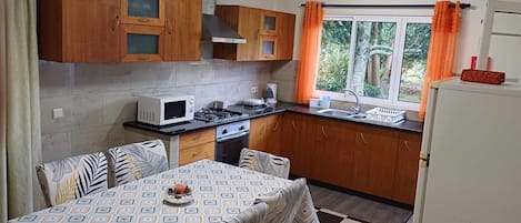 Una cocina compacta con muebles de madera, microondas, estufa y una mesa de comedor con sillas.