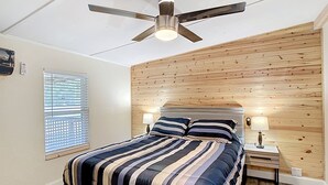 Une chambre à coucher avec un lit, un ventilateur de plafond, une table de chevet, une lampe et une fenêtre avec des stores.