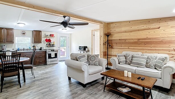 Un vaste salon avec un mur en bois, un ventilateur de plafond et un coin repas donnant sur une cuisine en arrière-plan.