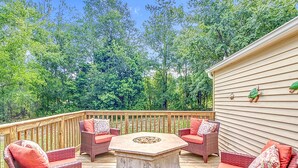 Une terrasse dotée de meubles en osier et d’une table en pierre, entourée d’une rambarde en bois et bordée d’arbres.