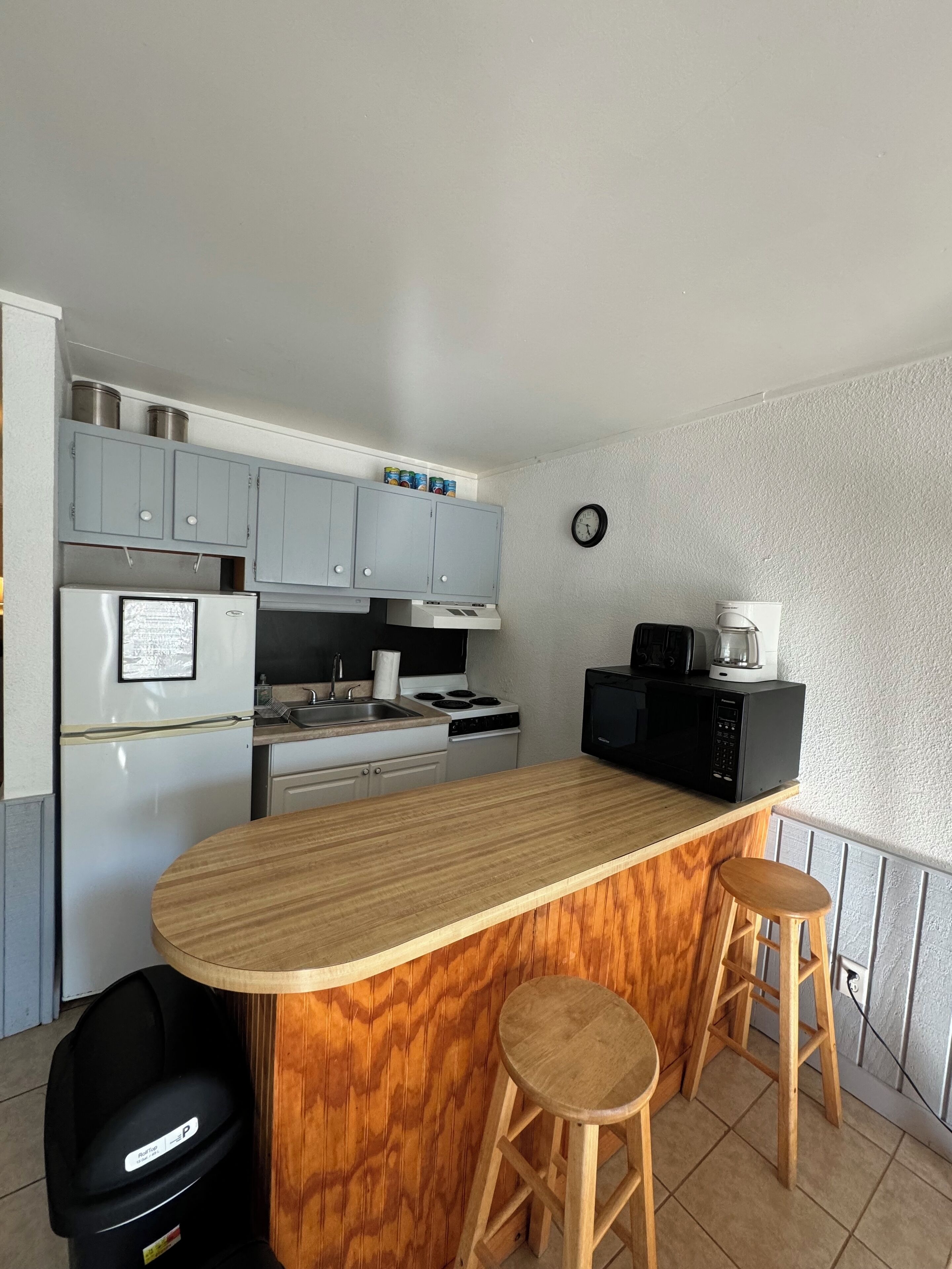 A compact kitchen with a wooden island, two stools, a refrigerator, a stove, and a microwave.