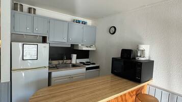 A compact kitchen with a wooden island, two stools, a refrigerator, a stove, and a microwave.