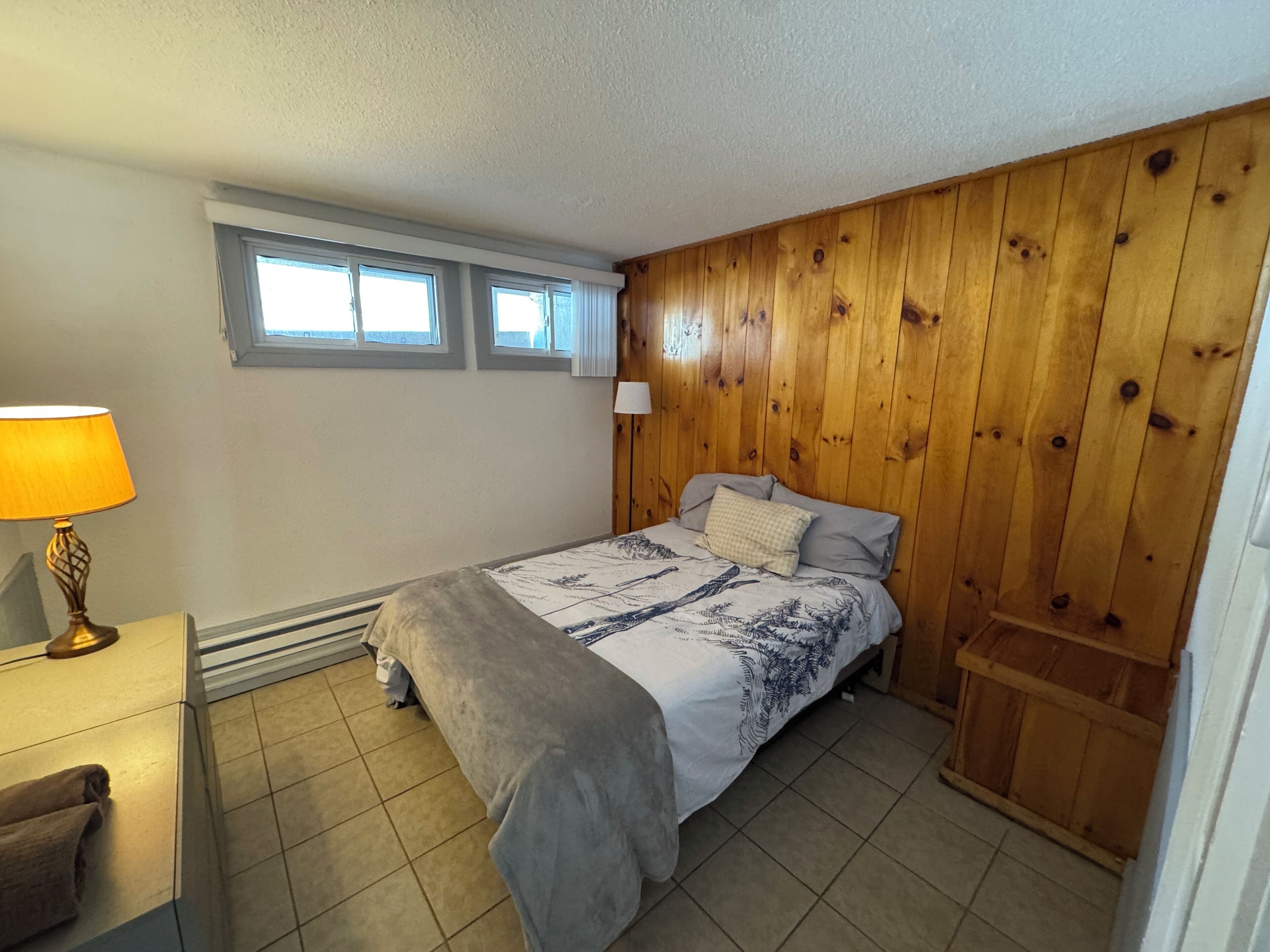Een slaapkamer met een bed, nachtkastje, lamp en raam.
