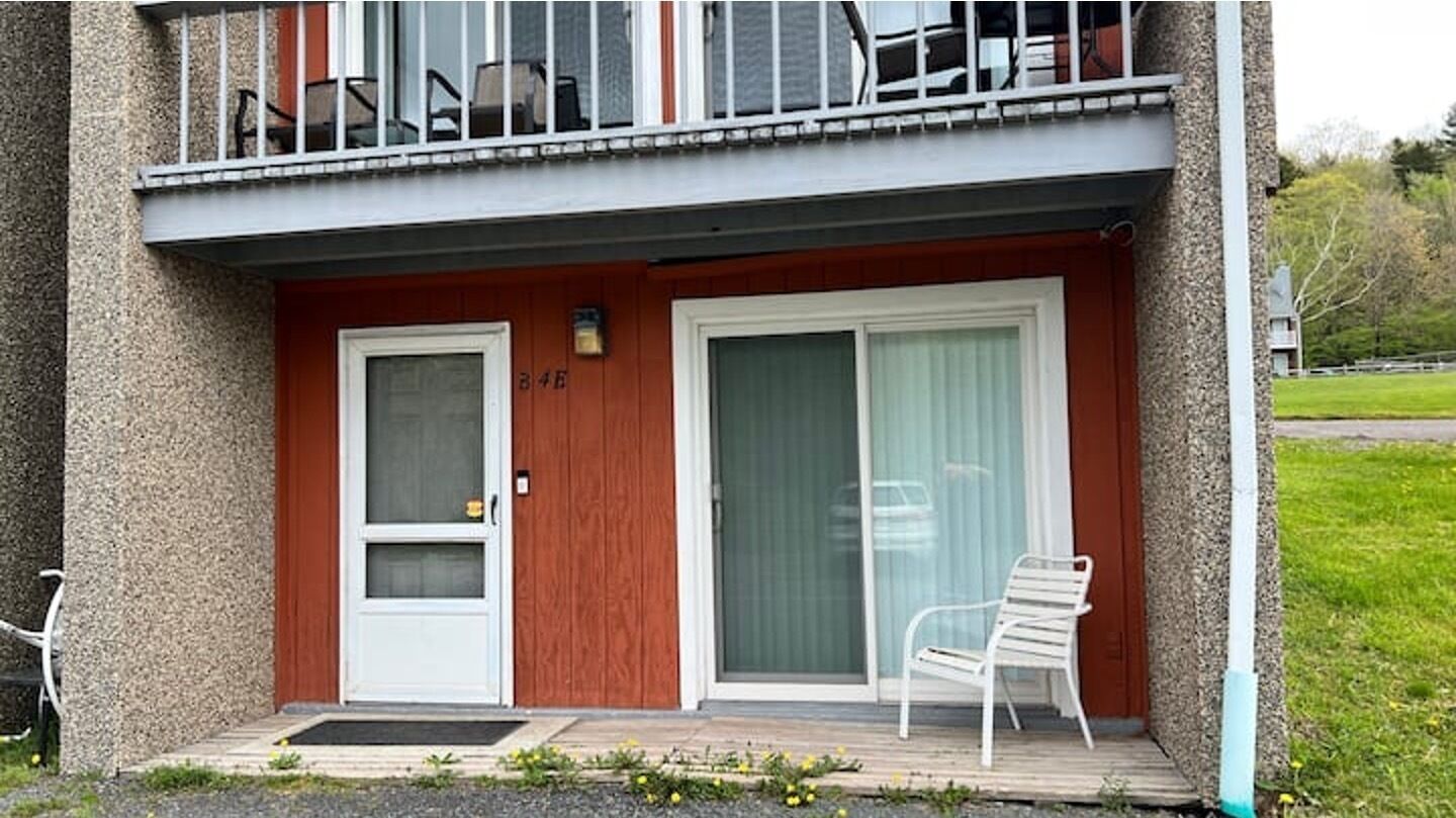 A two-story building with a red facade, a white door, and a large sliding glass door.
