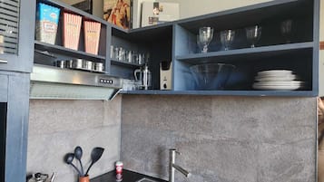 Een moderne keuken met een inbouwfornuis, een spoelbak en bovenkasten met keukengerei en decoratieve items.