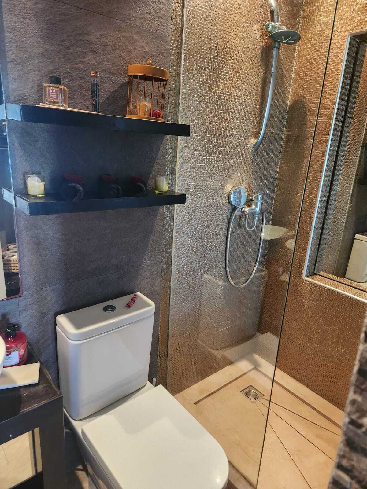 A modern bathroom with a glass-enclosed shower, a toilet, and a shelf with toiletries.