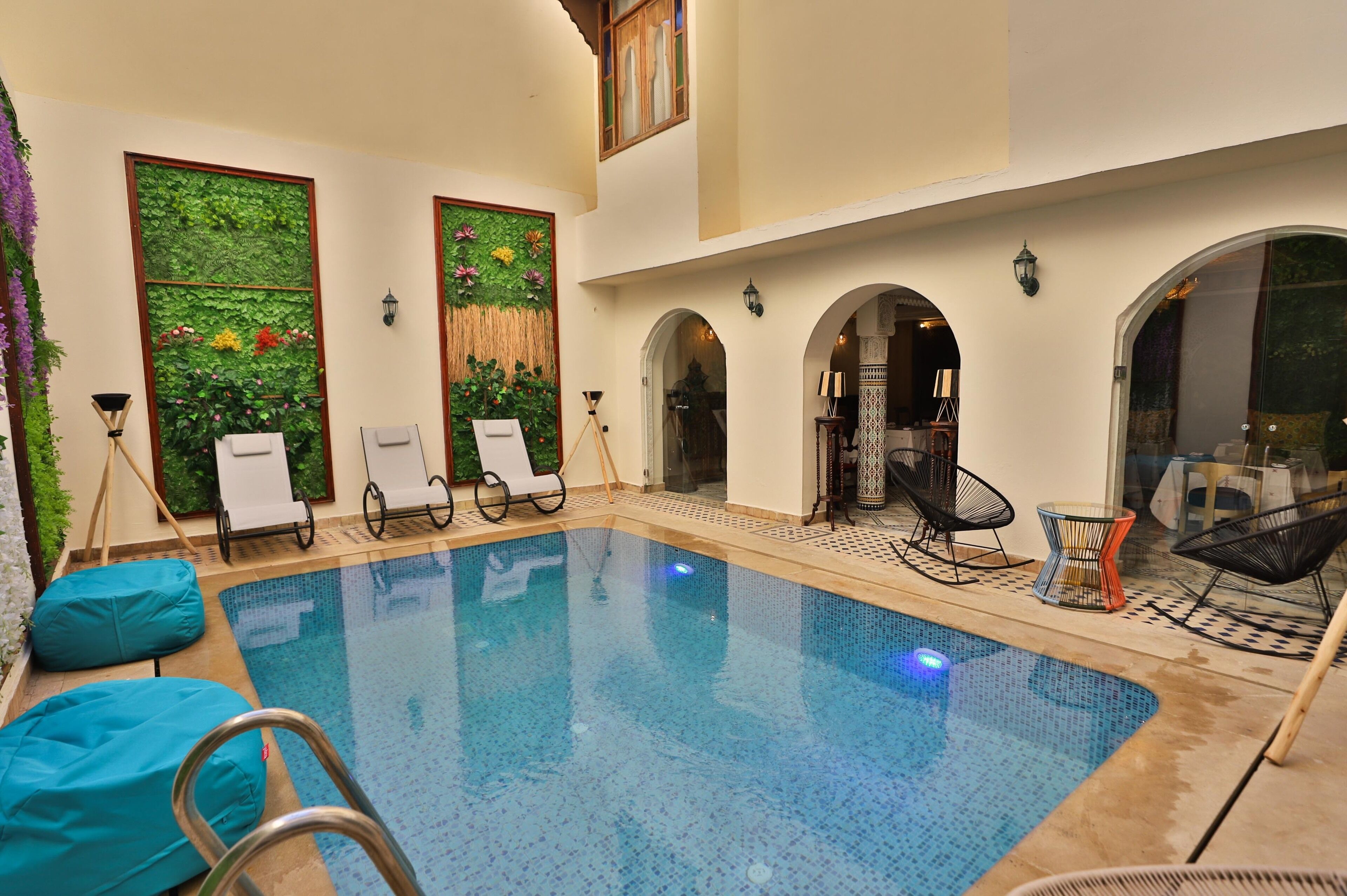 Une piscine intérieure dotée de chaises longues, d’une petite table et de panneaux muraux décoratifs.