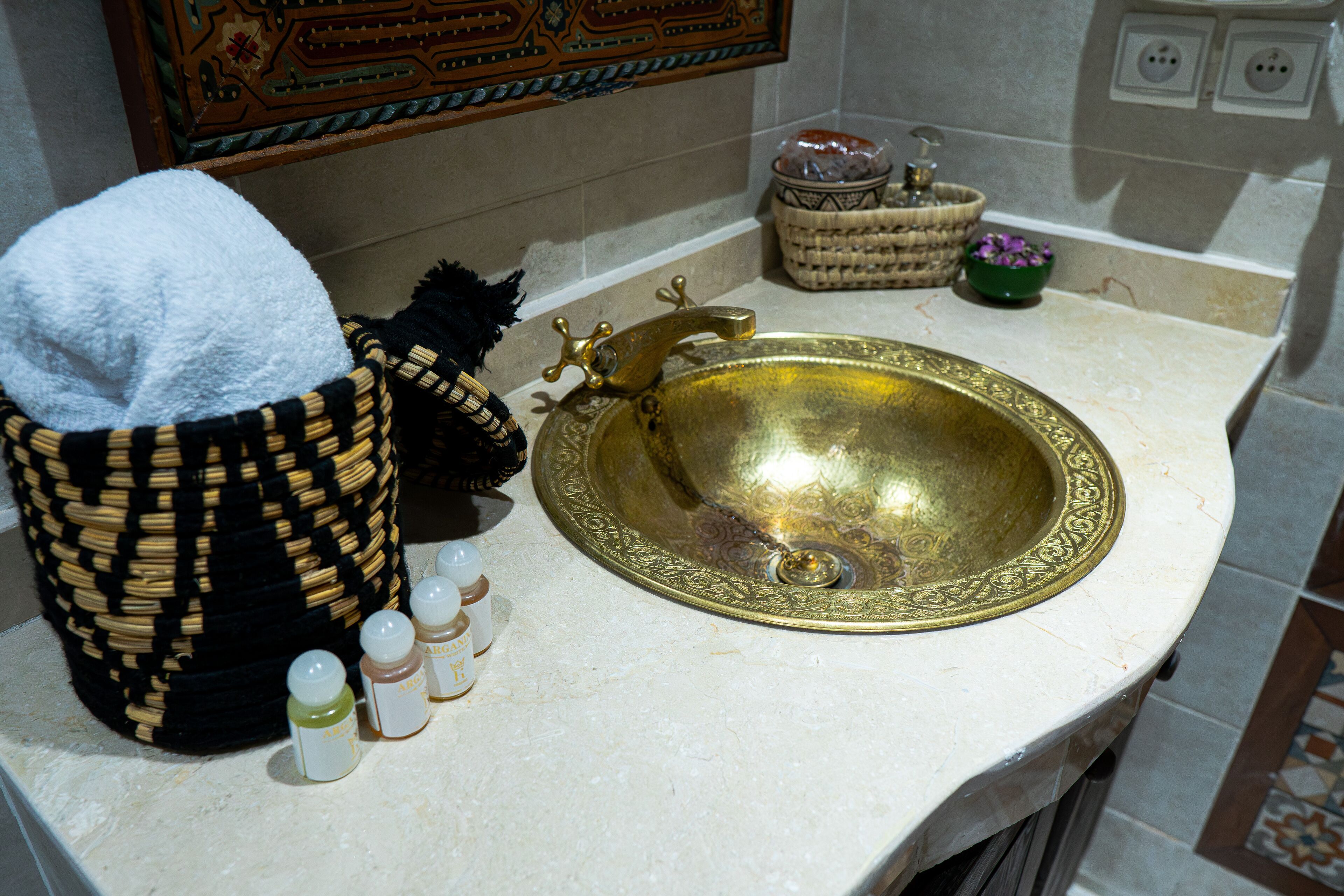 A bathroom with a brass sink, a woven basket, and toiletries.