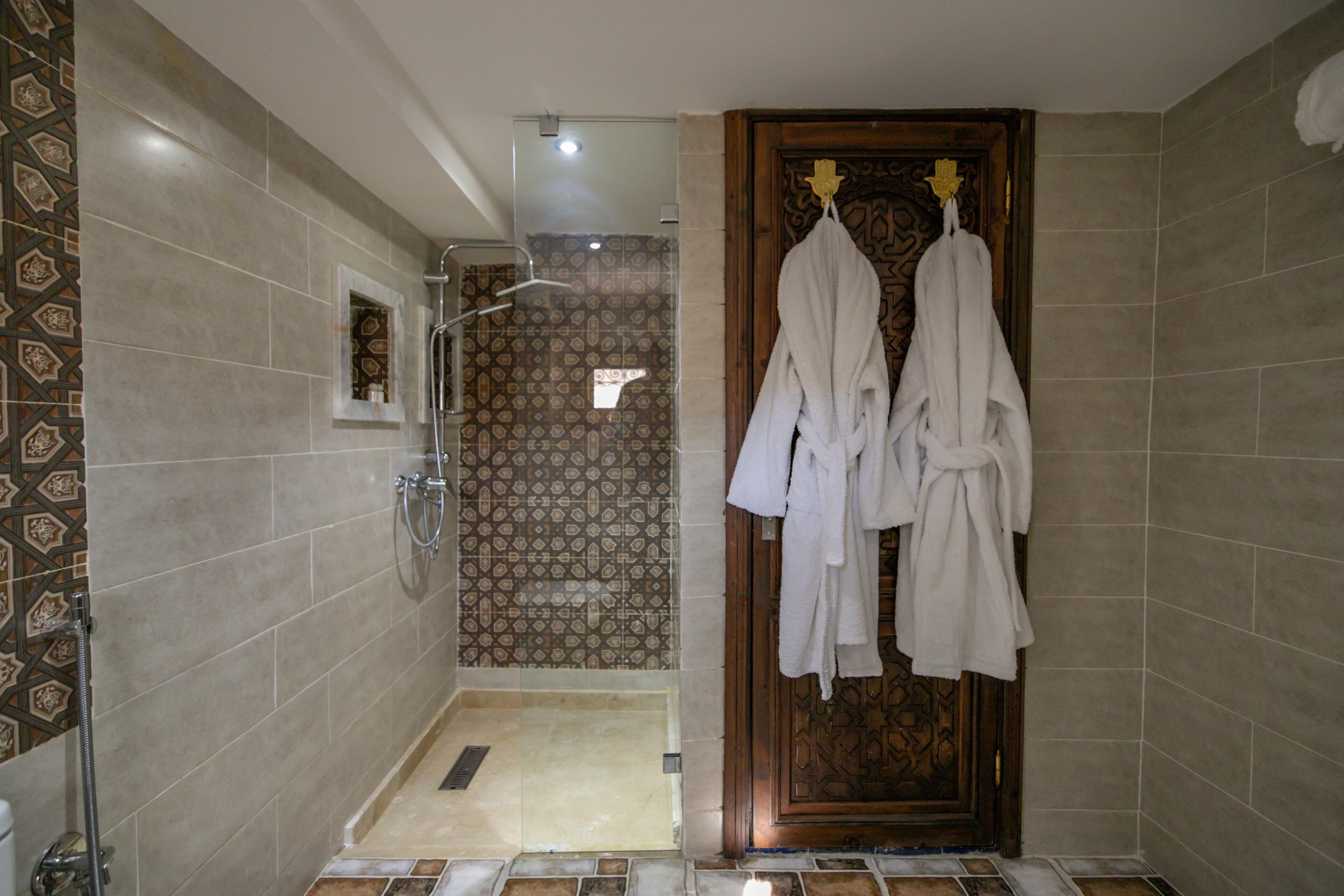 A bathroom with a shower, a towel rack with multiple towels, and patterned tiles on the walls.