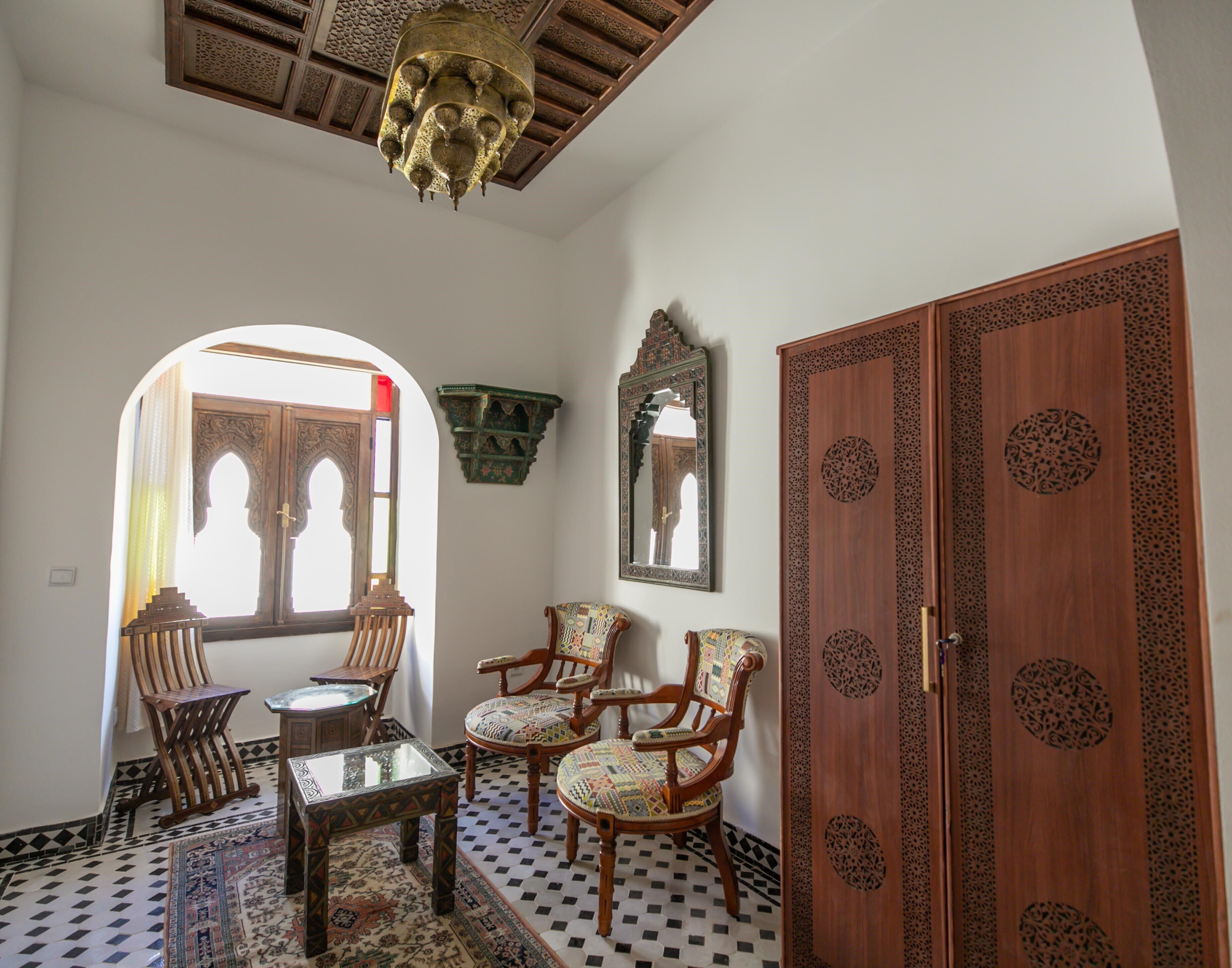 A room with a checkered floor, wooden furniture, a chandelier, and a large wooden door with intricate carvings.