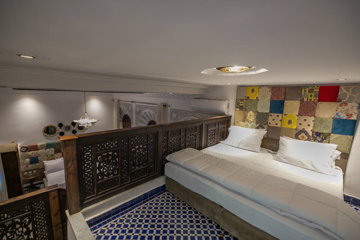 A bedroom with a bed, a decorative headboard, a blue and white tiled floor, and a wall with a patchwork design.