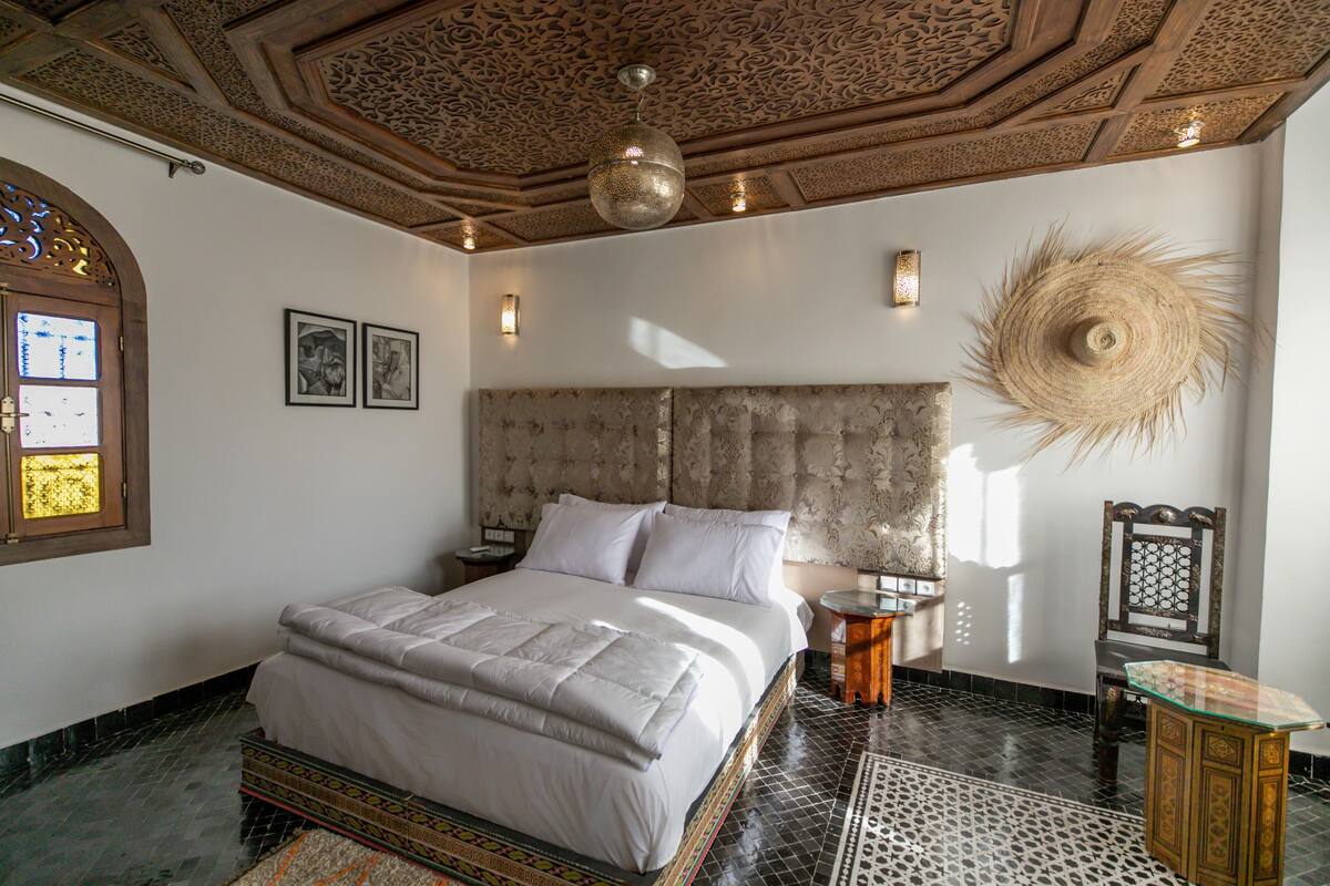 A bedroom with a large bed, a decorative ceiling, and a wall-mounted lamp.