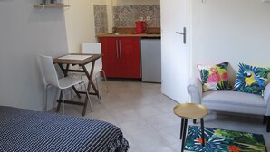 Ein kompakter Wohnbereich mit Küchenzeile, einem Essbereich mit Tisch und Stühlen sowie einer Couch mit bunten Kissen.