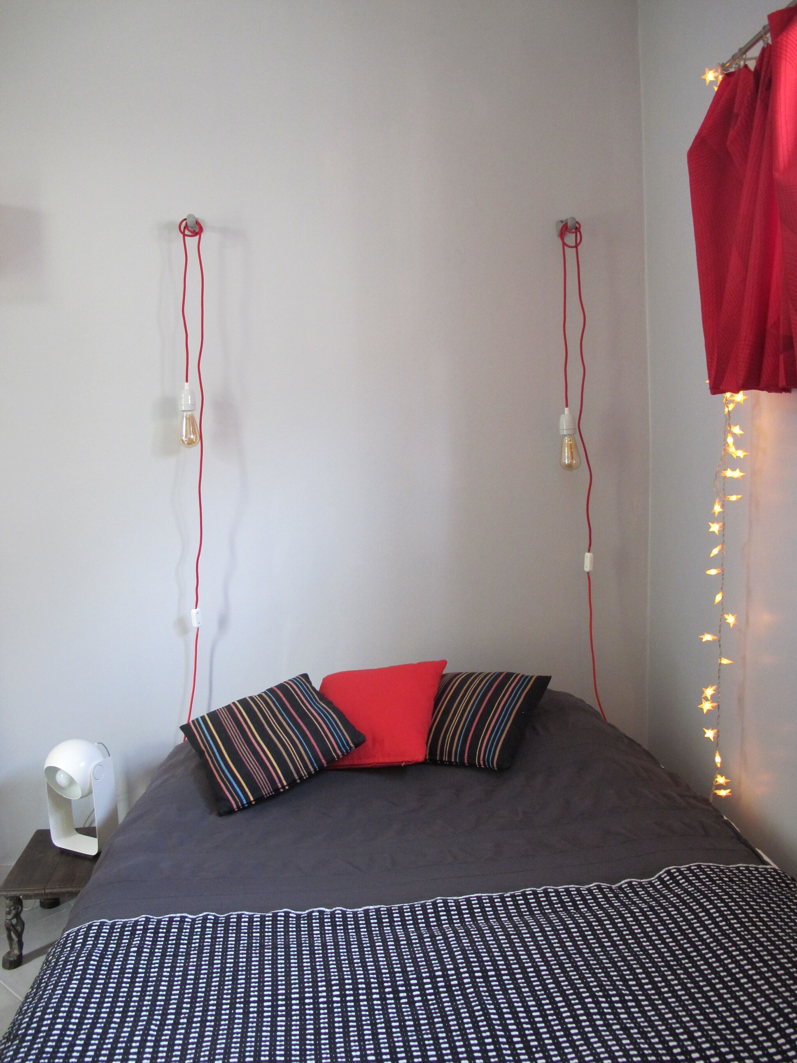 Een bed met een gebedruid sprei, twee kussens, een bedlampje en sprookjeslichtjes aan de muur.