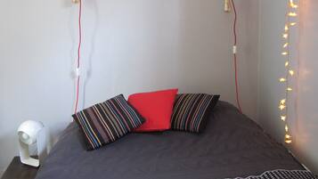 Een bed met een gebedruid sprei, twee kussens, een bedlampje en sprookjeslichtjes aan de muur.