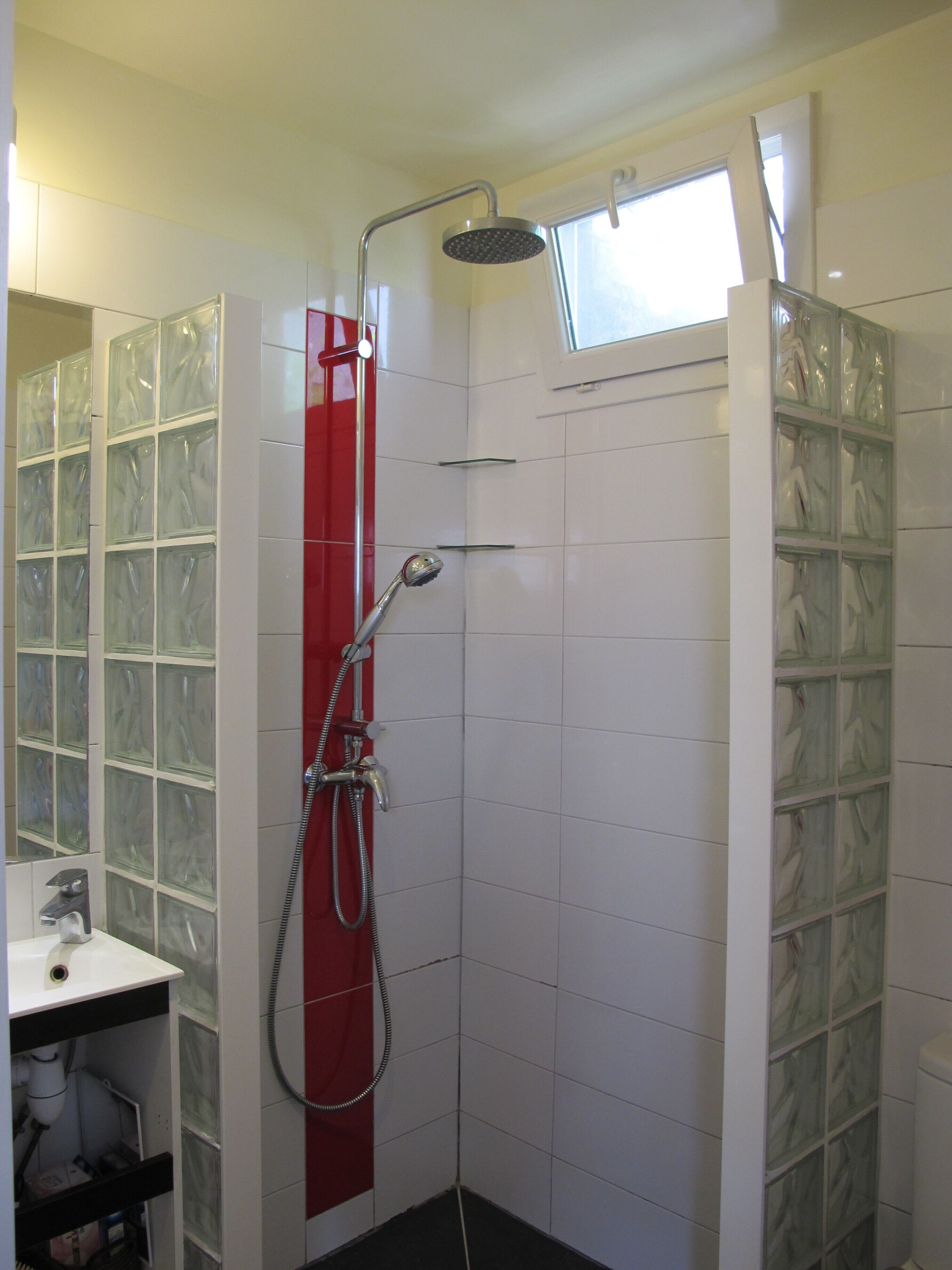 Een douche met glazen wand, een rode handdoekhouder en een raam boven de douche.