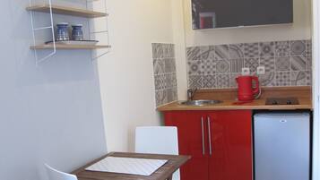 Een compacte keuken met een eethoek, bestaande uit een kleine tafel, stoelen, een koelkast en een plank met keukengerei.