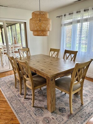 A dining area with a wooden table, six chairs, a woven pendant light, and patterned rugs. - Spacious Condo•Pond Views•Centrally located (Lewes)