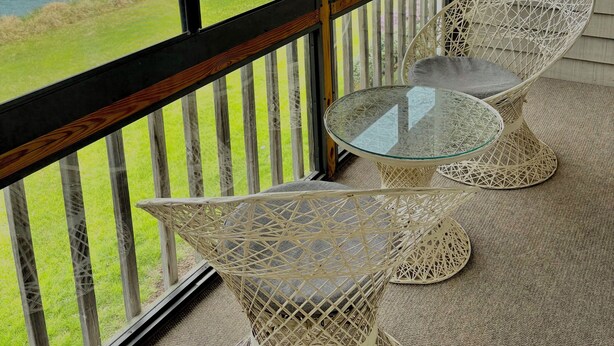 Une pièce dotée d’une grande fenêtre donnant sur une rivière, d’un fauteuil en osier et d’une table en verre.