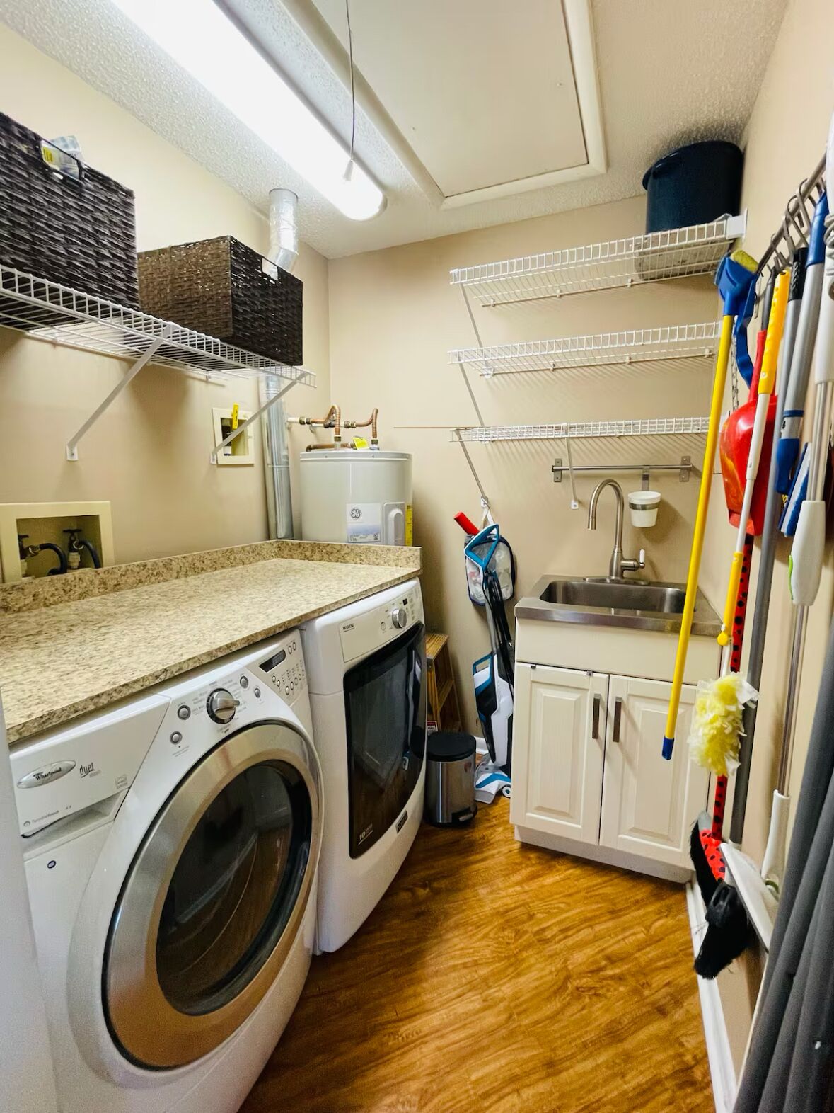 Une petite buanderie équipée d’un lave-linge, d’un sèche-linge et d’étagères superposées pour le rangement.
