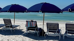 A beach with multiple blue umbrellas and metal chairs. - Sunrise Views at Boca Grande Waterfront Condo on Gasparilla Sound-BocaGrandeClub (Boca Grande)