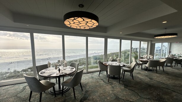A modern dining area with large windows offering ocean views, a round table with chairs, and a unique pendant light. - Sunrise Views at Boca Grande Waterfront Condo on Gasparilla Sound-BocaGrandeClub (Boca Grande)