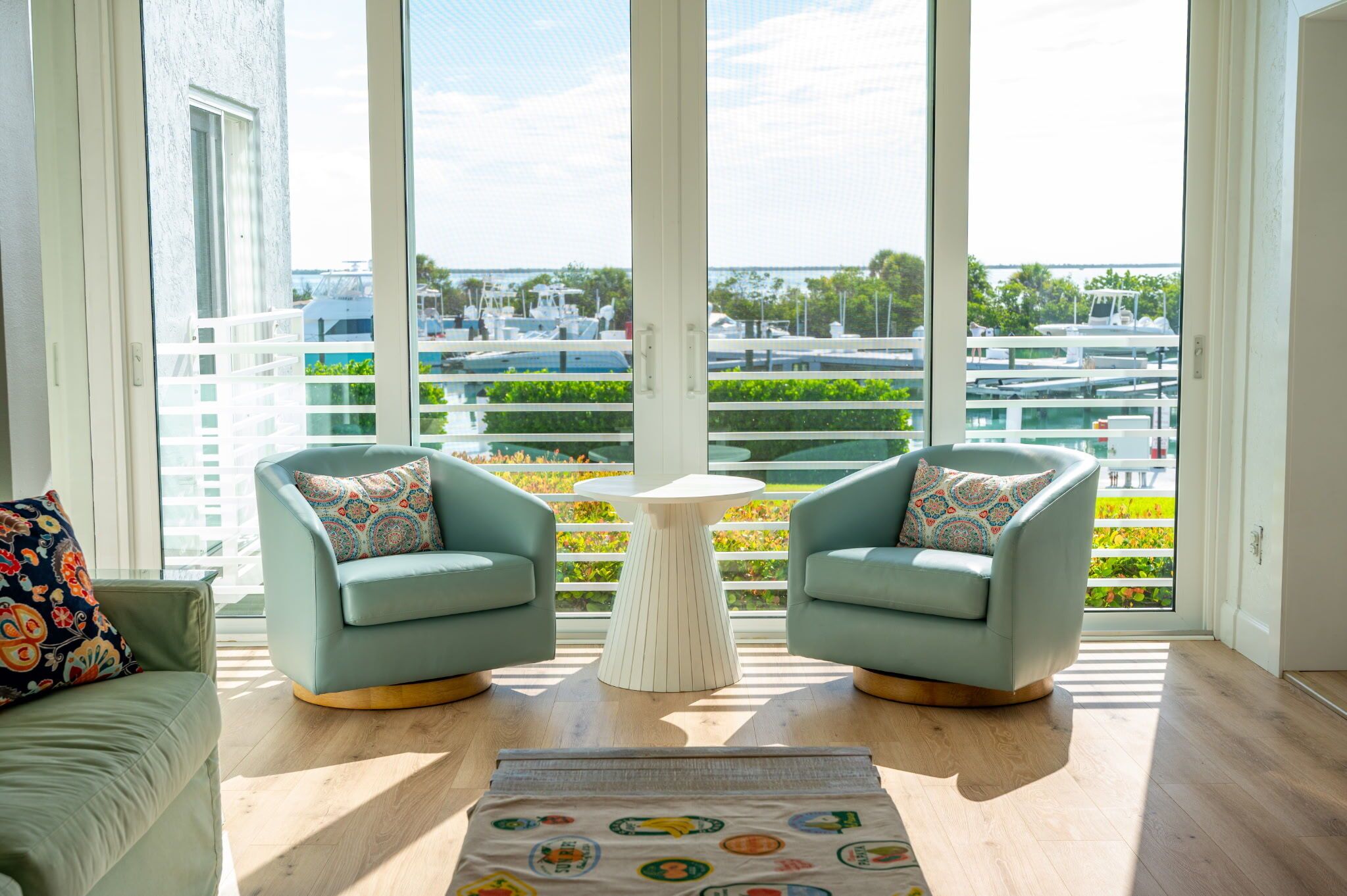 Un salon moderne avec deux fauteuils, une petite table ronde et une vue sur une marina, visible à travers de grandes fenêtres.