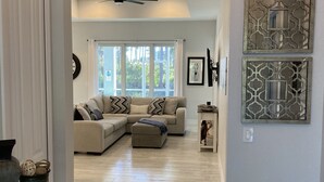 A spacious living room with a large sectional sofa, a glass coffee table, and decorative wall art. - New beautiful Pool .  May thru Dec 2025 $2599 a month.  $87a night. Contact Pam  (Rotonda West)