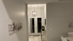 A hallway with a dining area, a door with a mirror, and a chandelier. - New beautiful Pool .  May thru Dec 2025 $2599 a month.  $87a night. Contact Pam  (Rotonda West)