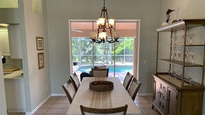 A dining area with a long table, chairs, a chandelier, a glass display case, and a view of a swimming pool. - South Venice Hidden Gem (Venice)
