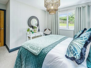 A bedroom with a bed, a bedside table, a mirror, and a window with curtains.