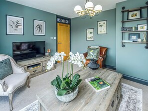 A living room with a TV, a coffee table with orchids, a leather armchair, and framed artwork on the walls.