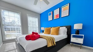 Une chambre à coucher moderne avec un lit noir, une literie blanche et un mur d’accent bleu.