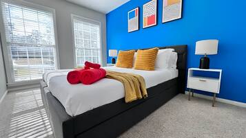 Une chambre à coucher moderne avec un lit noir, une literie blanche et un mur d’accent bleu.