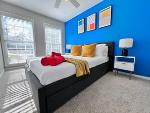A modern bedroom with a black bed, white bedding, and a blue accent wall.