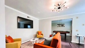 Un salon moderne avec une table de billard, deux fauteuils et un luminaire suspendu au plafond.
