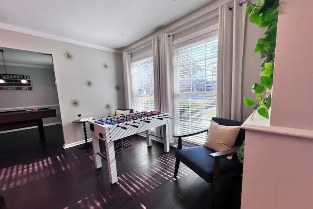 Une pièce équipée d’un baby-foot, d’une table de billard et d’une fenêtre avec des stores.