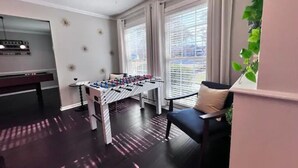 Une pièce équipée d’un baby-foot, d’une table de billard et d’une fenêtre avec des stores.