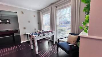 Une pièce équipée d’un baby-foot, d’une table de billard et d’une fenêtre avec des stores.