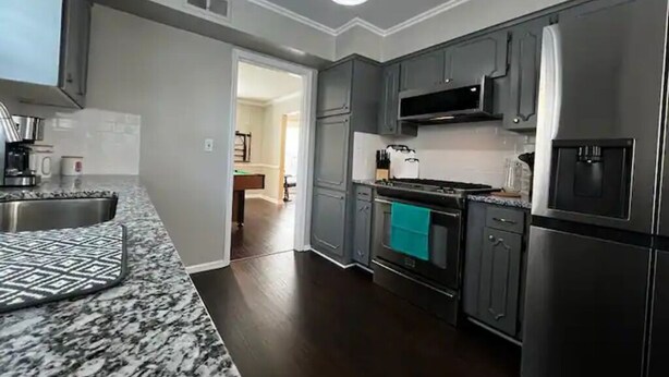 Une cuisine moderne avec des meubles de couleur sombre, des appareils en acier inoxydable et un dosseret décoré.
