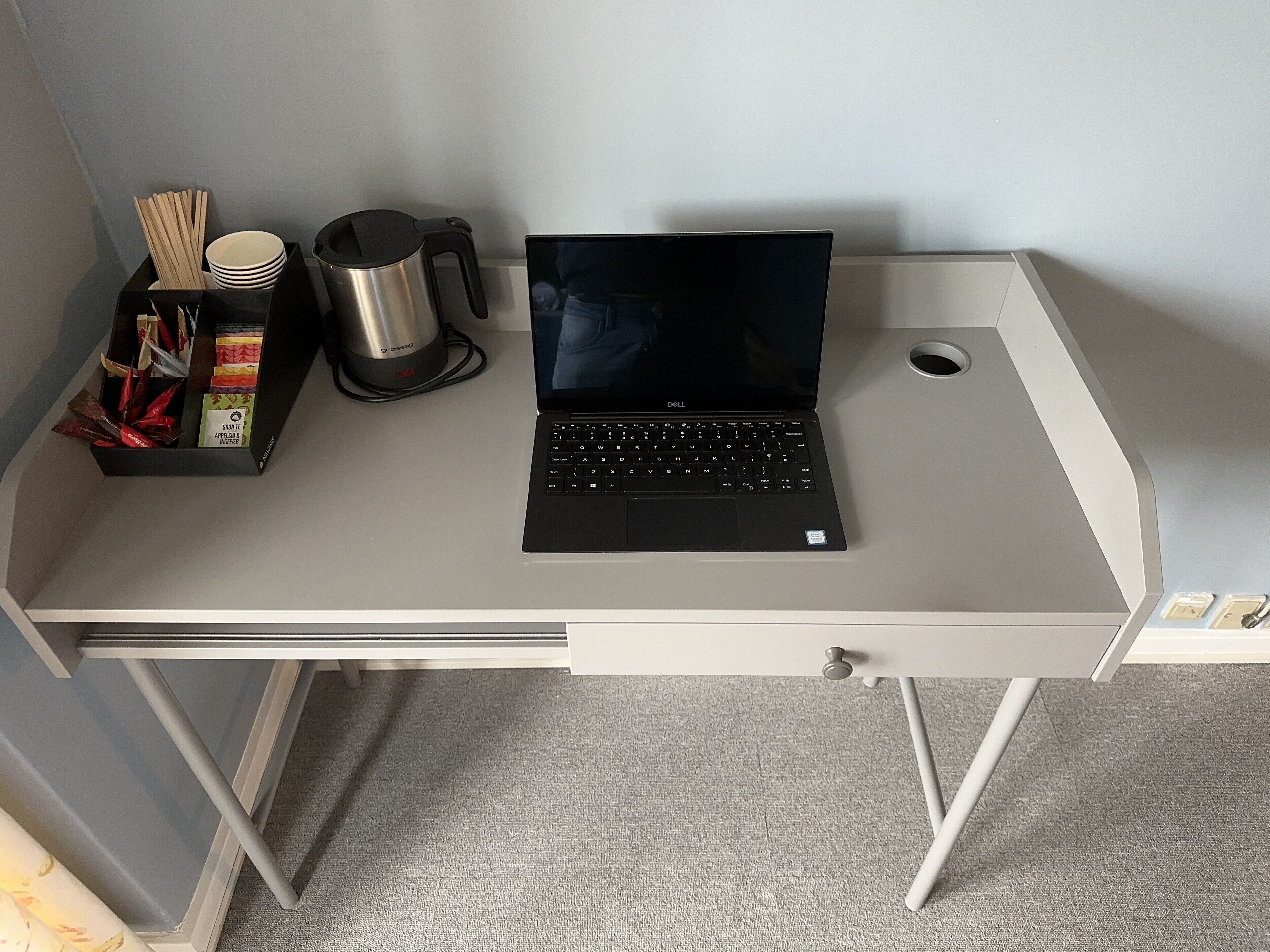 A laptop on a desk with a cup, chopsticks, and a box of snacks.
