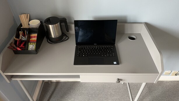 Una computadora portátil sobre un escritorio, con una taza, palillos y una caja de aperitivos.