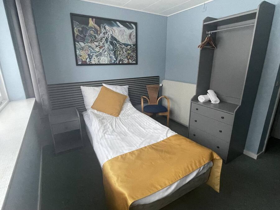 Ein Hotelzimmer mit Bett, Sessel, Kommode und einem Bild an der Wand.