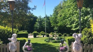 Un sendero de jardín con estatuas, una bandera y setos cuidados.