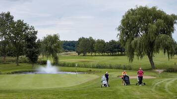 Un campo de golf con un estanque, árboles y una fuente.